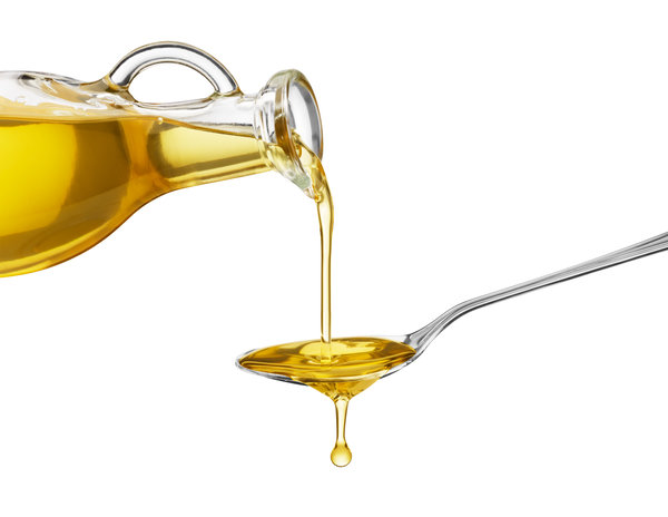 Herrliches Olivenöl wird aus einer Kanne auf einen Löffel gekippt.